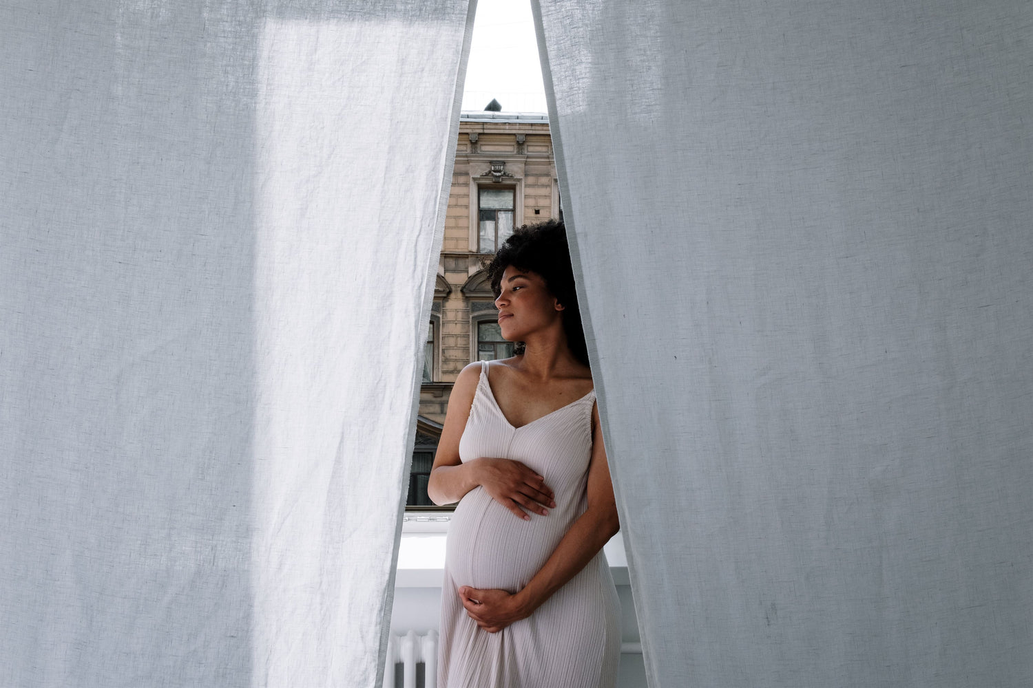 house of tallow mommy and baby product range pregnant woman in pink dress standing by the window